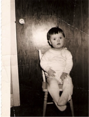 Black and white photograph of Robert as a boy sitting
        on a small wooden chair in front of a closed door. 