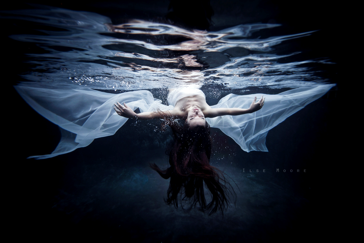 Figure 1. “The Immortal” by Ilse Moore (n.d.). Reprinted with
            permission. A female body lies just beneath the surface of a blackened
            water background. Her eyes are shut. Her face is turned up towards the
            surface and her arms are outstretched along her side. The woman is wrapped
            in a white chiffon scarf which floats around her arms like angel wings.